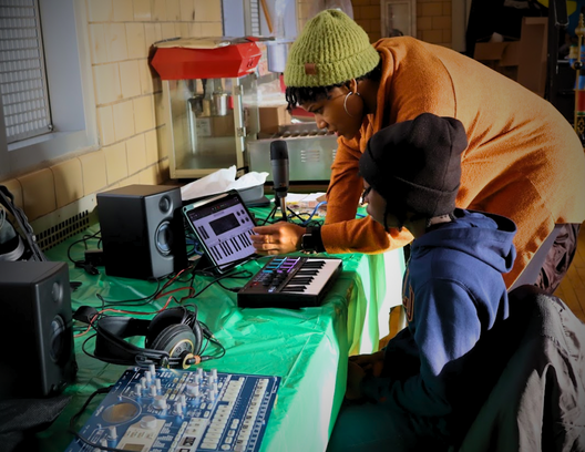 A teaching artist and a student at a keyboard, tablet, and studio speakers during Music Studio